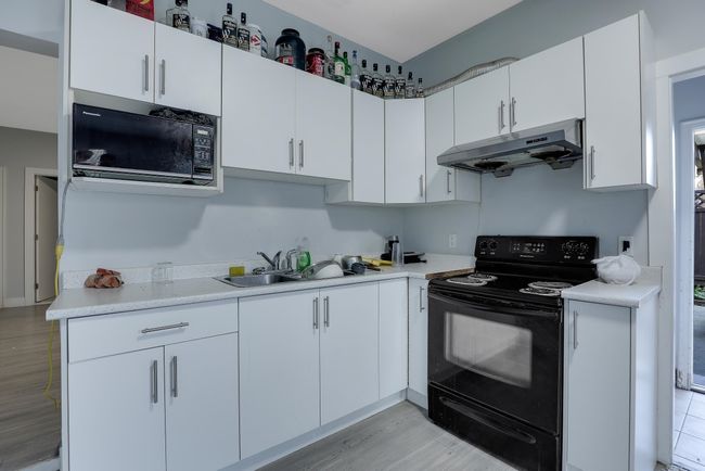 Kitchen featuring a sink, under cabinet range hood, light wood-type flooring, black appliances, and light countertops | Image 27