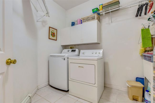 Laundry room featuring cabinets, washing machine and dryer, light tile patterned flooring, and a baseboard radiator | Image 12