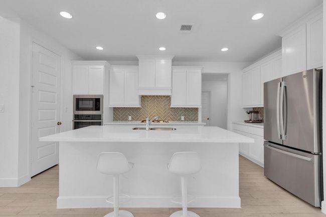 Kitchen featuring appliances with stainless steel finishes, an island with sink, white cabinetry, recessed lighting, and light countertops | Image 15