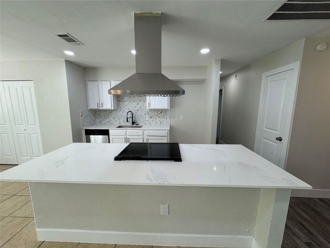 Kitchen featuring island exhaust hood, visible vents, dishwasher, a sink, and stovetop | Image 9