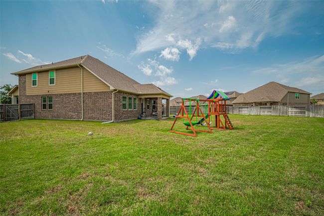 A spacious backyard with well-maintained grass, featuring a colorful play set. The house has a brick exterior and a fenced perimeter, offering privacy and a safe play area. | Image 47