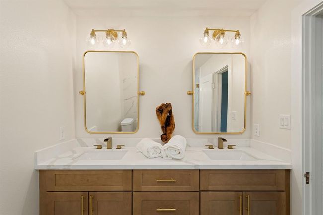 The primary ensuite bathroom offers dual sinks complimented by stunning gold pivot framed mirrors and elegant vanity lighting. Ample storage can be utilized via the large under-cabinets and centered drawers. | Image 21