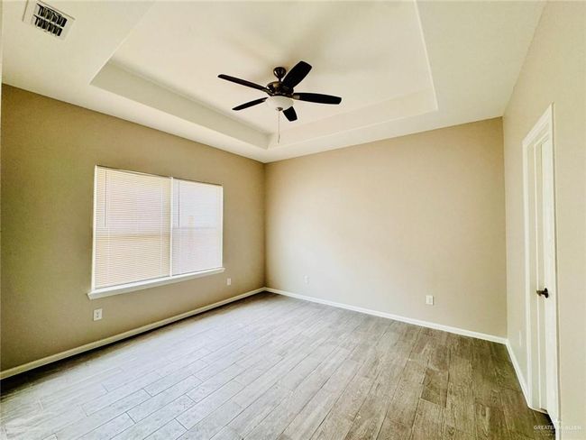 Empty room with a tray ceiling, wood finished floors, and a ceiling fan | Image 8