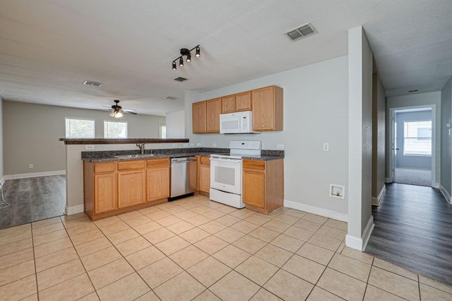 Kitchen with white appliances, a peninsula, a ceiling fan, rail lighting, and light tile patterned floors | Image 7