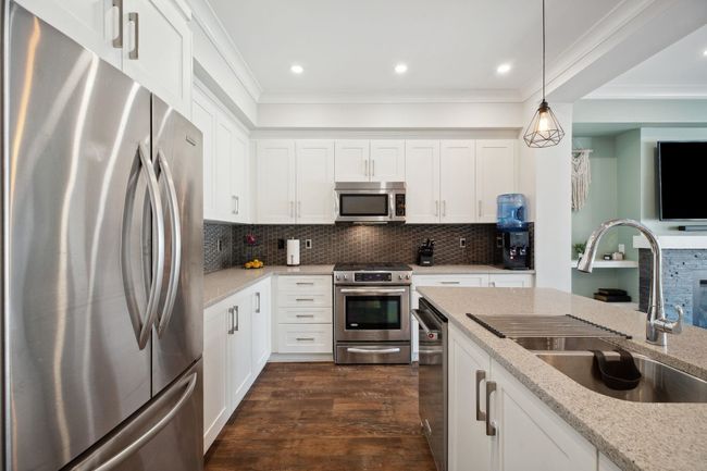 Kitchen featuring a sink, ornamental molding, dark wood-style flooring, appliances with stainless steel finishes, and decorative backsplash | Image 13