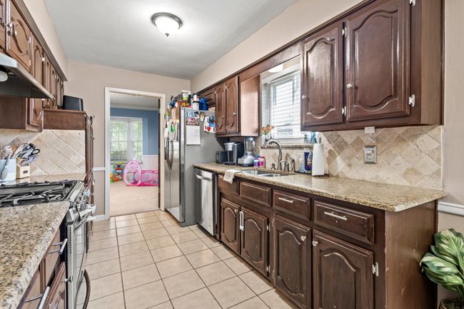 Kitchen with appliances with stainless steel finishes, dark brown cabinetry, light tile patterned floors, backsplash, and extractor fan | Image 6