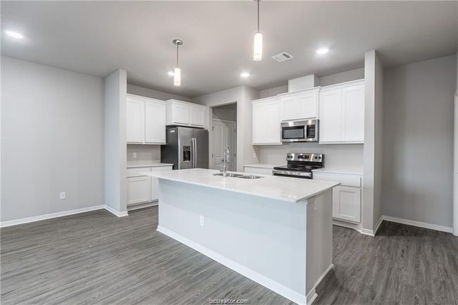Kitchen featuring stainless steel appliances, sink, decorative light fixtures, white cabinets, and a center island with sink | Image 4