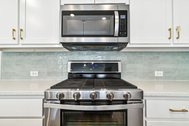 Kitchen with stainless steel appliances, white cabinetry, backsplash, and light stone countertops | Image 15