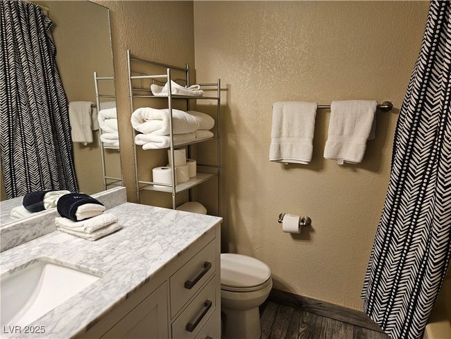Bathroom with wood finished floors, vanity, a textured wall, and curtained shower | Image 7