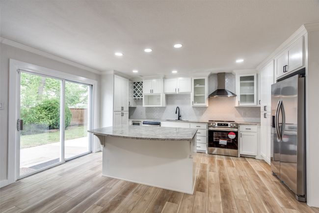 Kitchen with appliances with stainless steel finishes, wall chimney exhaust hood, ornamental molding, light wood-type flooring, and backsplash | Image 14