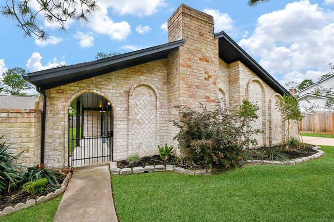 Charming brick home with arched entryway and landscaped front yard. Features a gated walkway and lush greenery, providing a welcoming and secure atmosphere. | Image 9