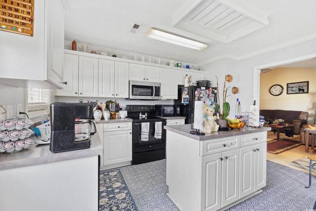 Kitchen featuring electric range, stainless steel microwave, freestanding refrigerator, white cabinets, and crown molding | Image 4