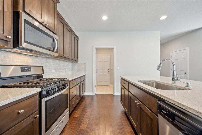 Kitchen featuring light stone countertops, a sink, dark wood finished floors, appliances with stainless steel finishes, and backsplash | Image 8
