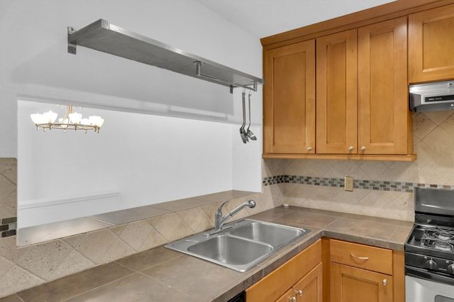 Kitchen with under cabinet range hood, gas stove, backsplash, a sink, and brown cabinets | Image 5