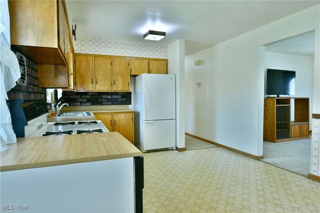 Kitchen with a sink, brown cabinets, white appliances, light colored carpet, and baseboards | Image 14