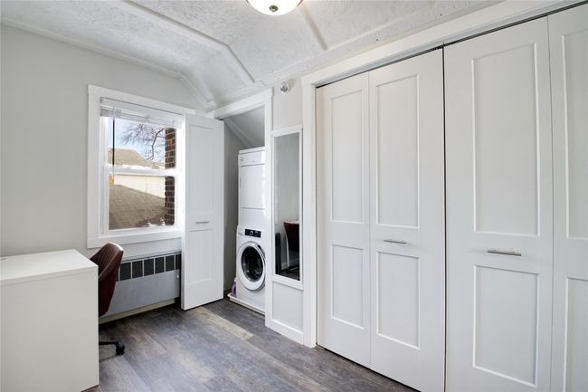 Laundry area with stacked washer / drying machine, wood finished floors, an office area, and a textured ceiling | Image 13