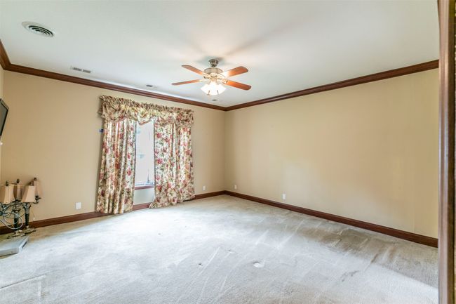 Carpeted empty room with crown molding, a ceiling fan, and visible vents | Image 11