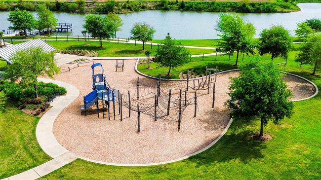 This photo showcases a scenic playground next to a lake, featuring a climbing structure, slide, and a picnic area. Surrounded by lush greenery and walking paths, it's an ideal spot for family activities and relaxation. | Image 48