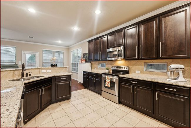 Kitchen with stainless steel appliances, tasteful backsplash, ornamental molding, light tile patterned floors, and dark brown cabinets | Image 8