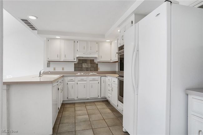 Kitchen with under cabinet range hood, light countertops, visible vents, a sink, and white appliances | Image 15