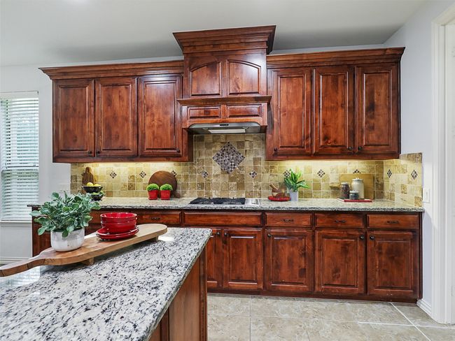 Kitchen featuring stainless steel gas stovetop, light stone counters, and tasteful backsplash | Image 10