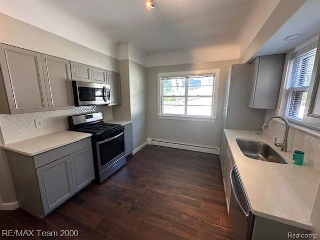 Kitchen with gray cabinets, stainless steel appliances, backsplash, light stone countertops, and baseboard heating | Image 15