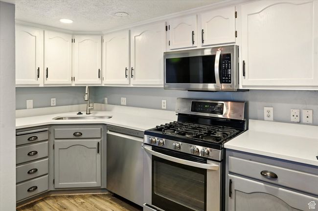 Kitchen featuring stainless steel appliances, gray cabinetry, a sink, light wood-type flooring, and light countertops | Image 10