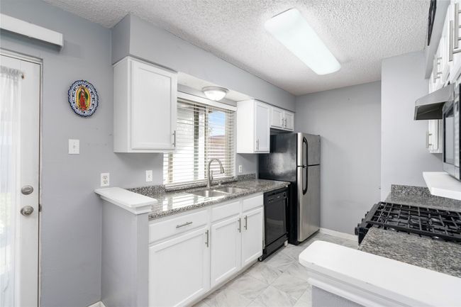Kitchen with sink, white cabinetry, stone countertops and black dishwasher | Image 13