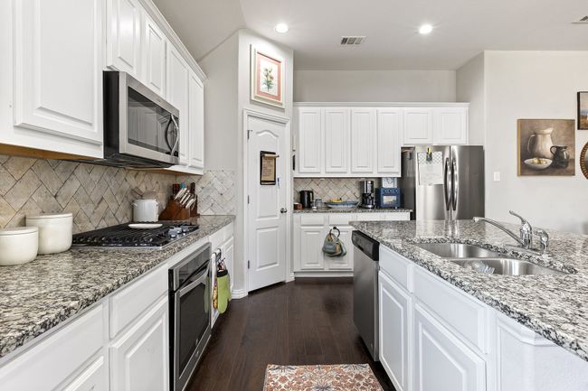 Kitchen featuring white cabinets, stainless steel appliances, a sink, visible vents, and dark wood-type flooring | Image 12