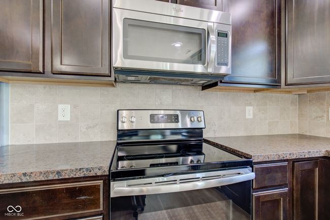 kitchen featuring appliances with stainless steel finishes, dark brown cabinetry, backsplash, and dark countertops | Image 10