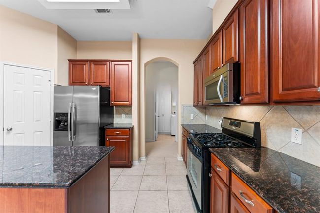 This well-equipped kitchen features rich wood cabinetry, granite countertops, and stainless steel appliances—including a gas cooktop for precise, efficient cooking. | Image 10