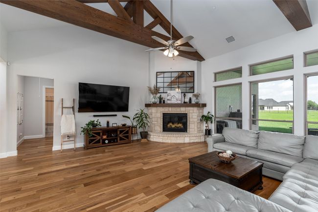 Living area featuring high vaulted ceiling, ceiling fan, a fireplace, beamed ceiling, and wood finished floors | Image 8