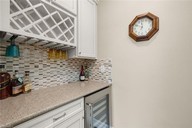 Bar featuring white cabinets, decorative backsplash, light stone counters, and beverage cooler | Image 14