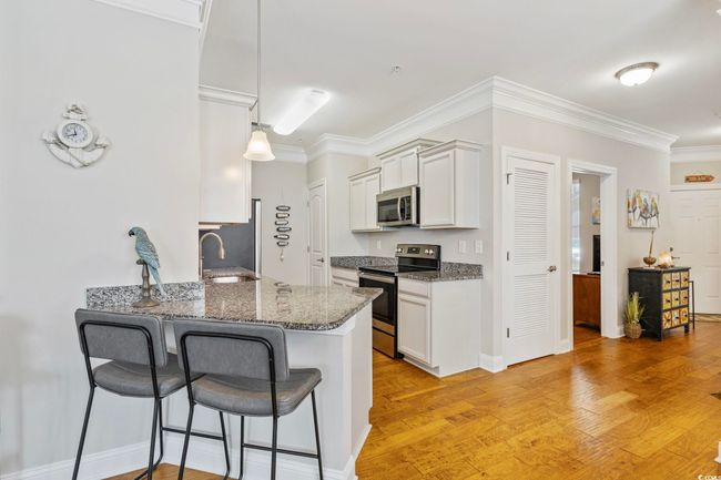 Kitchen with appliances with stainless steel finishes, a kitchen bar, dark stone countertops, a peninsula, and white cabinets | Image 9