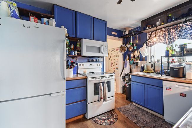 Kitchen with white appliances, blue cabinetry, a sink, and wood finished floors | Image 20