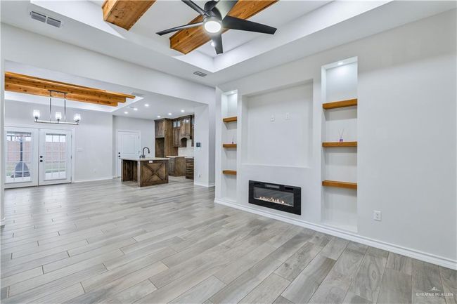 Unfurnished living room with a ceiling fan, light wood-type flooring, a glass covered fireplace, beam ceiling, and a raised ceiling | Image 4