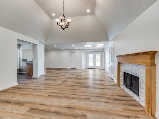 Unfurnished living room featuring a stone fireplace, high vaulted ceiling, light wood-style flooring, a chandelier, and recessed lighting | Image 8