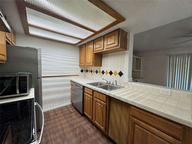 Kitchen with appliances with stainless steel finishes, dark wood-style flooring, tasteful backsplash, brown cabinets, and a peninsula | Image 7