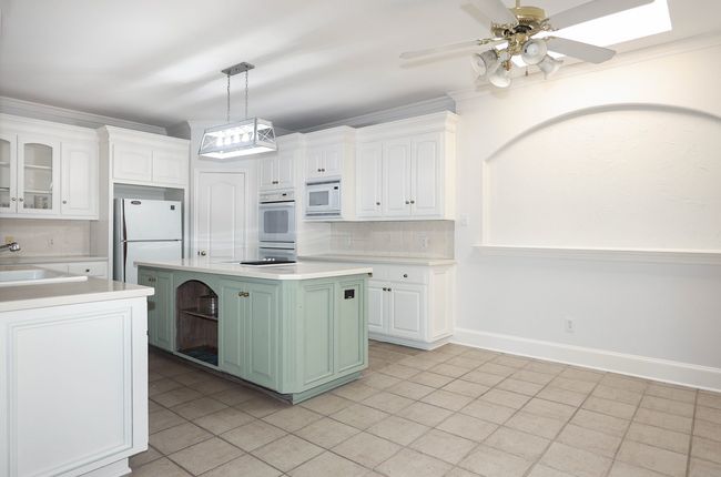 Kitchen with tasteful backsplash, white cabinets, a sink, light countertops, and white appliances | Image 4
