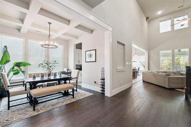 Dining space featuring dark wood-style floors, beam ceiling, a chandelier, coffered ceiling, and a high ceiling | Image 6