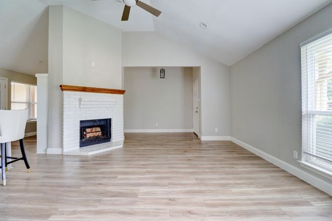 Unfurnished living room with ceiling fan, vaulted ceiling, a fireplace, and light wood-type flooring | Image 4