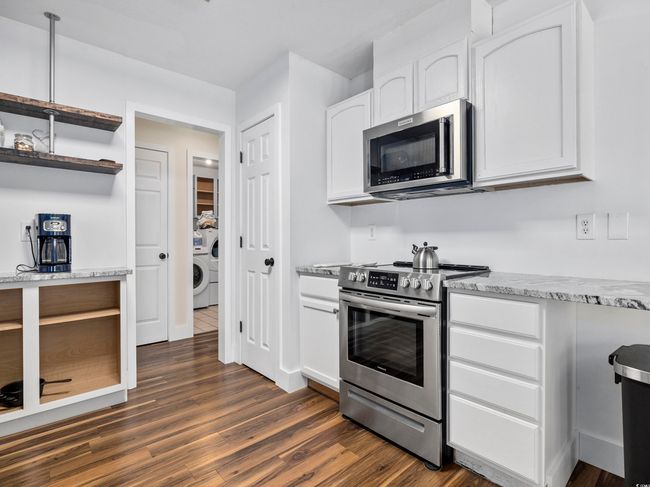 Kitchen with white cabinets, dark wood-style flooring, open shelves, appliances with stainless steel finishes, and washer / clothes dryer | Image 11