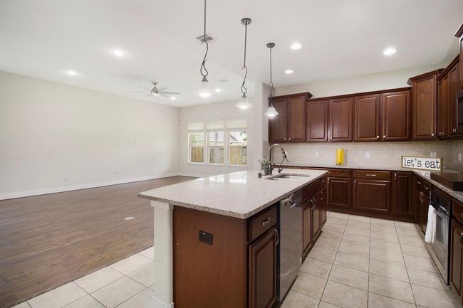 A spacious open-concept kitchen and living area. The kitchen features upgraded cabinetry, granite countertops, and modern appliances, with ample natural light from large windows. | Image 10