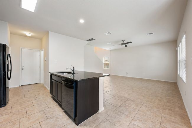 Kitchen featuring a sink, dishwashing machine, black fridge with ice dispenser, ceiling fan, and light tile patterned floors | Image 18
