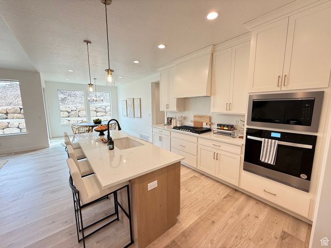 Kitchen featuring a sink, appliances with stainless steel finishes, light wood-type flooring, a center island with sink, and custom range hood | Image 7