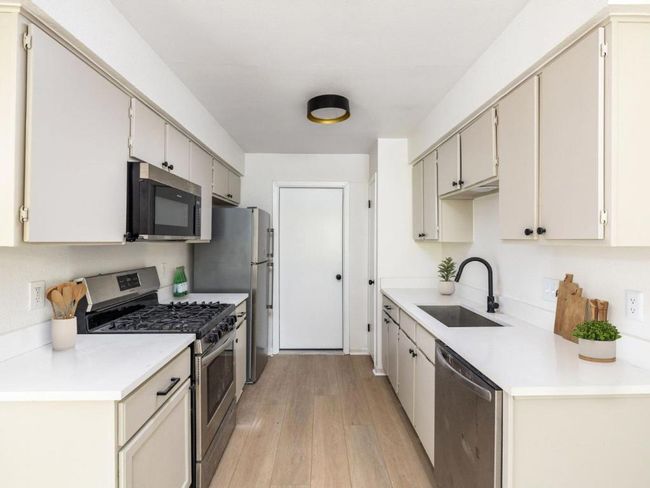 Kitchen with stainless steel appliances, a sink, light wood-style floors, and light countertops | Image 12