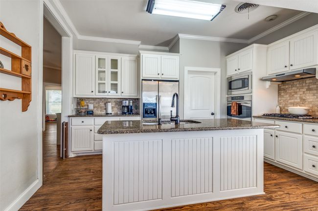 The kitchen has been thoughtfully updated with granite countertops, classic beadboard cabinetry, a large center island with built-in sink, and stainless steel appliances—including gas cooktop, built-in oven and microwave. | Image 9
