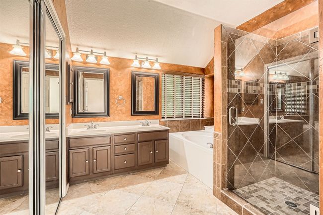 Full bathroom featuring double vanity, a bath, a stall shower, lofted ceiling, and a textured ceiling | Image 15
