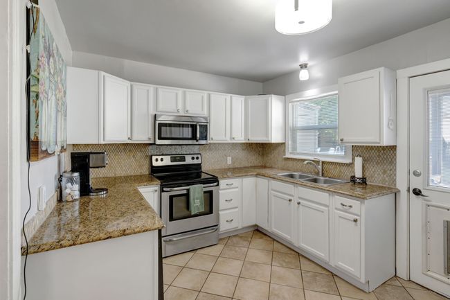 Kitchen with light tile patterned flooring, stainless steel appliances, white cabinetry, and sink | Image 8