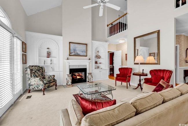 Carpeted living room featuring high vaulted ceiling, built in shelves, a ceiling fan, and a glass covered fireplace | Image 5